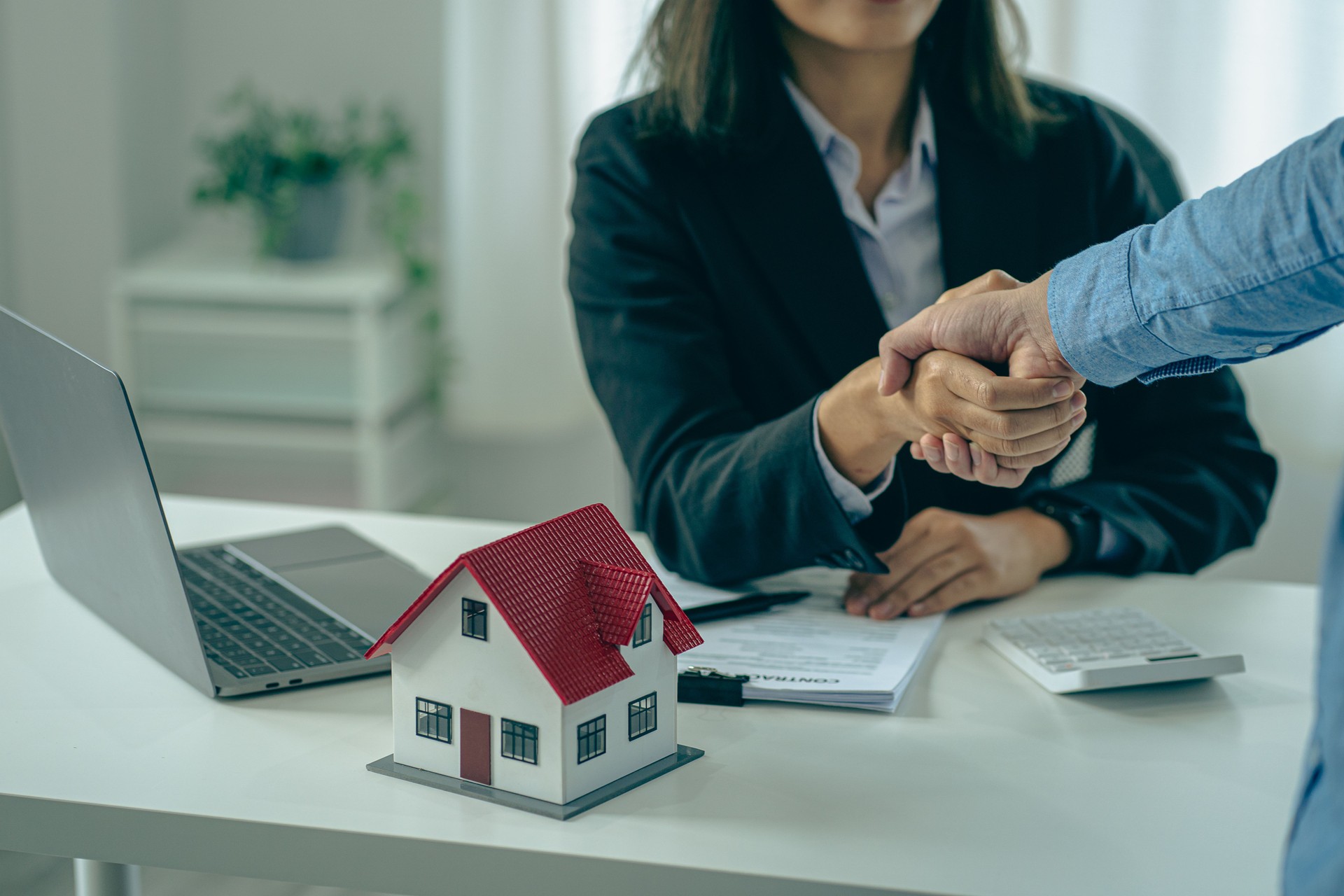 Sales agents and landlords when signing a contract to buy or rent a new home. Real estate agents shake hands with customers after signing contracts. Contract documents and house plans on a wooden table