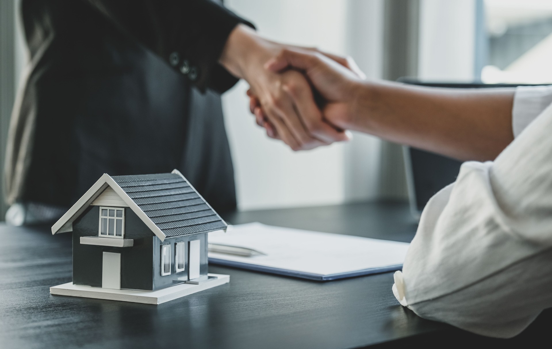 Home model. Real estate agents and buyers handshake after signing a business contract, renting, buying, mortgage, loan or home insurance